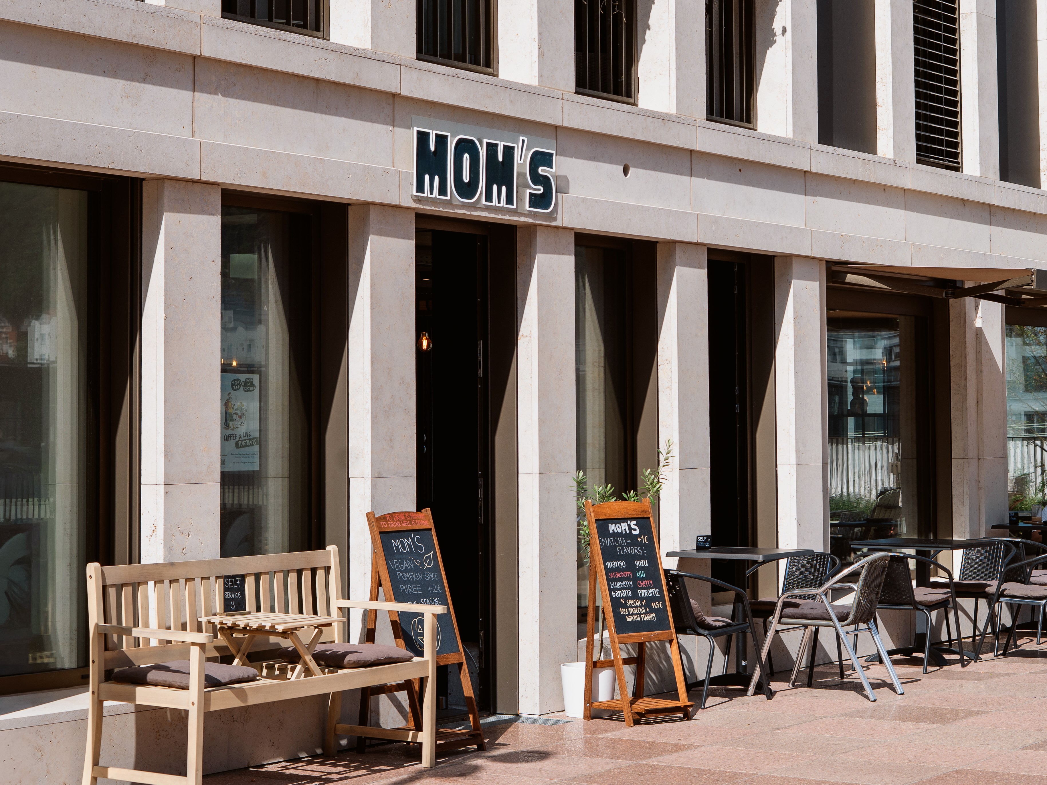 Eingang von Mom's Café & Bar mit Sitzbank und Kreidetafeln